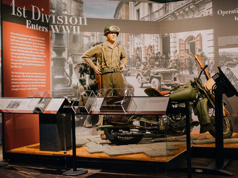 1st Division Enters WWII museum exhibit including a mannequin Soldier and motorcycle.